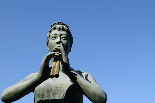 Statue of a woman playing a flute against a clear blue sky.