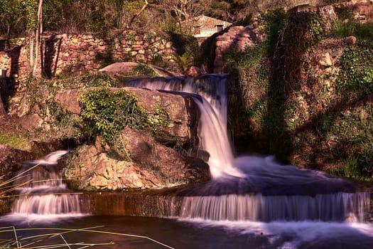 Small waterfalls in a mountain stream on a sunny day.long exposure. Mystic, vegetation, stone walls, lonely, empty space, romantic, idyllic.