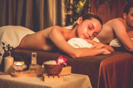 Caucasian couple customer enjoying relaxing anti-stress spa massage and pampering with beauty skin recreation leisure in warm candle lighting ambient salon spa at luxury resort or hotel. Quiescent