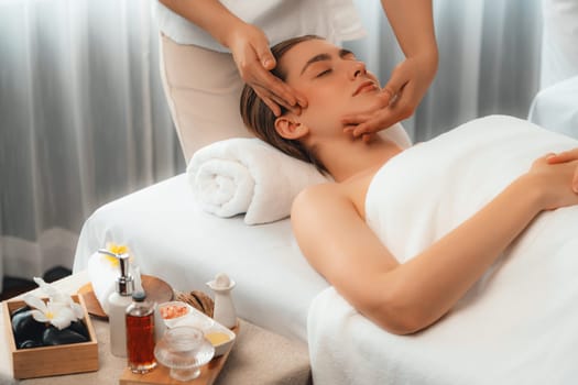 Caucasian woman enjoying relaxing anti-stress head massage and pampering facial beauty skin recreation leisure in dayspa modern light ambient at luxury resort or hotel spa salon. Quiescent