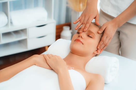 Caucasian woman enjoying relaxing anti-stress head massage and pampering facial beauty skin recreation leisure in dayspa modern light ambient at luxury resort or hotel spa salon. Quiescent