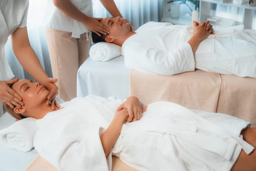 Caucasian couple enjoying relaxing anti-stress head massage and pampering facial beauty skin recreation leisure in dayspa modern light ambient at luxury resort or hotel spa salon. Quiescent