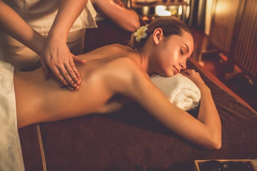 Caucasian couple customer enjoying relaxing anti-stress spa massage and pampering with beauty skin recreation leisure in warm candle lighting ambient salon spa at luxury resort or hotel. Quiescent