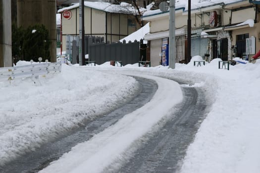 Winding road covered in snow in a quiet urban area with buildings and snowbanks on the sides.