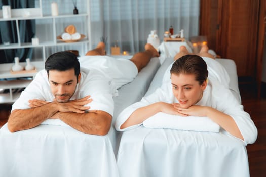 Caucasian couple customer enjoying relaxing anti-stress spa massage and pampering with beauty skin recreation leisure in day light ambient salon spa at luxury resort or hotel. Quiescent