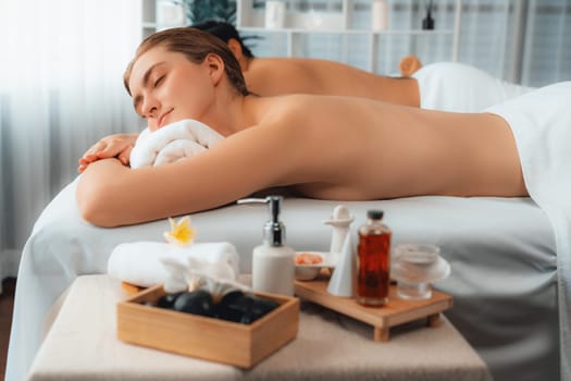 Caucasian couple customer enjoying relaxing anti-stress spa massage and pampering with beauty skin recreation leisure in day light ambient salon spa at luxury resort or hotel. Quiescent