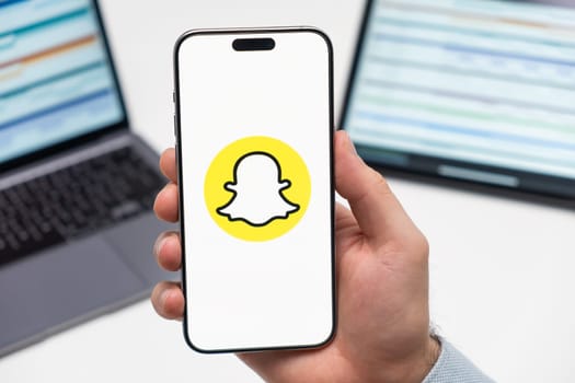 Snapchat logo of social media application on the screen of smart phone in mans hand, laptop and tablet on the background