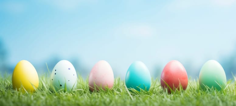 A vibrant row of painted Easter eggs in shades of yellow, blue, pink, and green nestled in green grass under a clear blue sky.