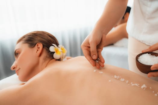 Blissful couple customer having exfoliation treatment in luxury spa salon with warmth candle light ambient. Salt scrub beauty treatment in health spa body scrub. Quiescent
