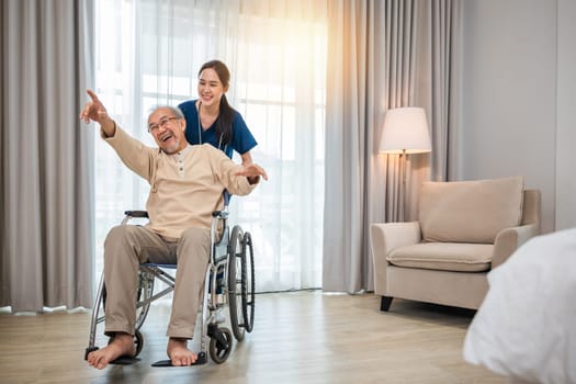Happy curator person doctor pushing and walk elderly patient freedom raising arm at hospital, Asian senior retired old man sitting on wheelchair having fun with young woman nurse, disabled sanatorium