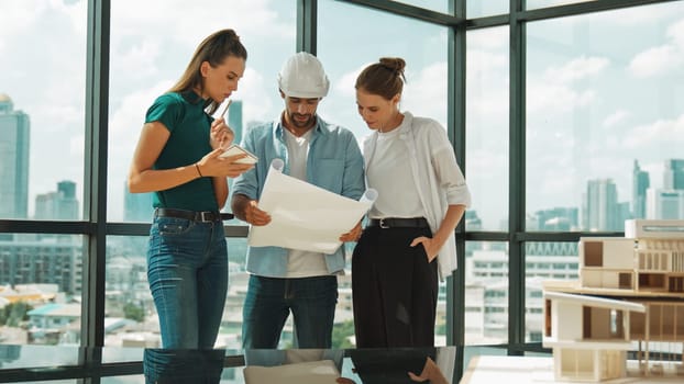 Professional architect engineer team talking, sharing, brainstorming about design while manager hold at project plan. Young architect holding plan while manager listen and point at plan. Tracery