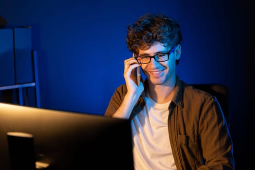 Young businessman calling on smartphone to customer or coworker, looking at computer screen of creative presentation surround work desk at neon modern office. Concept of new next project. Gusher.