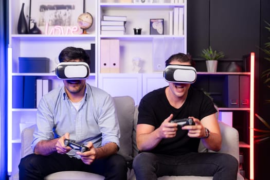 Buddy friend gamers playing video game using joysticks and VR headset of virtual technology in reality in studio room with neon blue light. Comfy living indoor with cheerful fighting winner. Sellable.