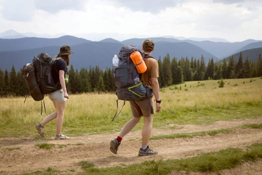 A young happy couple in love, a guy and a girl with a tourist backpack and equipment go on a trip, walk along trails, forest and mountains , friends actively spend time together in nature outdoor.