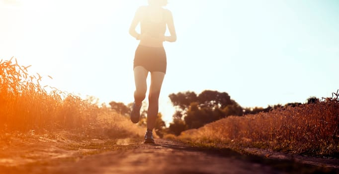 Young sports girl in a top and shorts trains outdoors, runs at sunset. A woman is engaged in trail running outdoor, preparing for a long race, enjoys an active lifestyle.