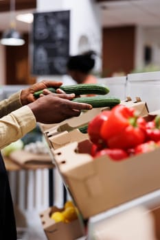 African American owner arranging eco friendly groceries. Customers select healthy fruits and vegetables, glass jars, and bulk items. Indoor modern supermarket with a focus on local produce.