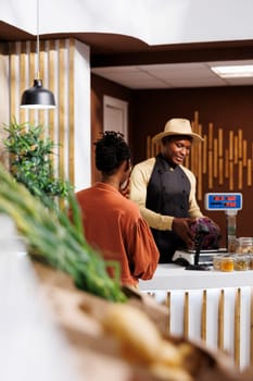 While shopping for fresh products, a black woman is helped by a male vendor. The shopkeeper provides a choice of vivid and healthful alternatives, resulting in a pleasant shopping experience.