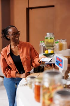 African American woman making contactless payment at grocery food market using her smartphone. Convenient wireless technology for cashless checkout for customer at local eco friendly store.