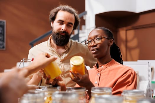 Close-up of multicultural couple in a plastic free convenience store, looking at glass jars of honey. African American girlfriend and her Caucasian boyfriend are shopping sustainably at local shop.