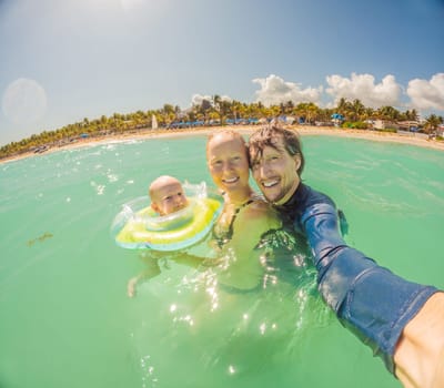 Adorable baby swims in an inflatable ring around his neck, enjoying the sea with his mom and dad.
