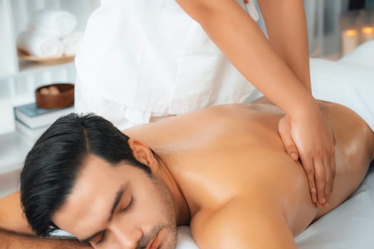 Caucasian man customer enjoying relaxing anti-stress spa massage and pampering with beauty skin recreation leisure in day light ambient salon spa at luxury resort or hotel. Quiescent