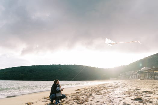 Dad with a little girl flying a kite sitting on the beach by the sea. High quality photo