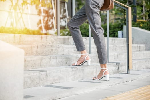 Businesswoman in modern suit is captured in moment of ambition climbing city stairs. Her black shoe-clad foot symbolizes relentless effort and progress embodying spirit of success in corporate world.