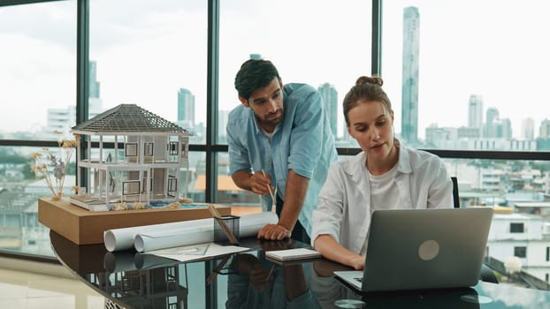 Smart architect engineer inspect house model while colleague using laptop analysis data. Professional designer team working together to design house model construction at modern office. Tracery