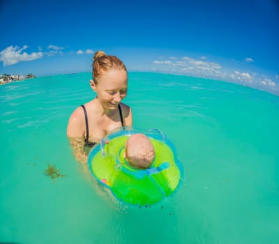 Adorable baby swims in an inflatable ring around his neck, enjoying the sea with his mom