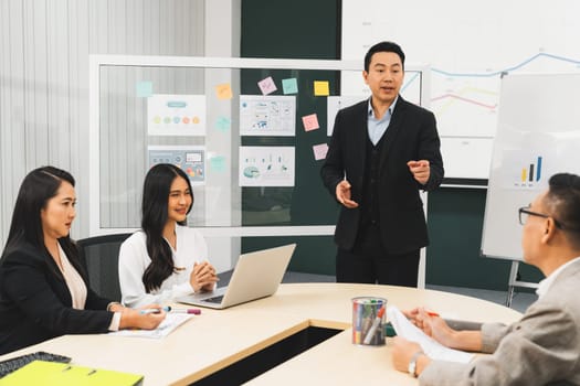 Successful businessmen present financial projects on glass whiteboard confidently. Executive managers listen to employee's quarterly business plan presentation. Modern meeting room. Intellectual.
