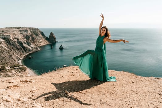 Woman green dress sea. Female dancer posing on a rocky outcrop high above the sea. Girl on the nature on blue sky background. Fashion photo