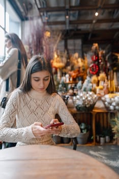 With a phone in hand, a young lady browses the decor shop. High quality photo