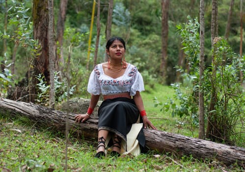 beautiful young woman from otavalo, ecuador resting in a forest on a tree trunk. indigenous woman with traditional dress, woman enjoying the harmony and peace of nature. earth day. High quality photo