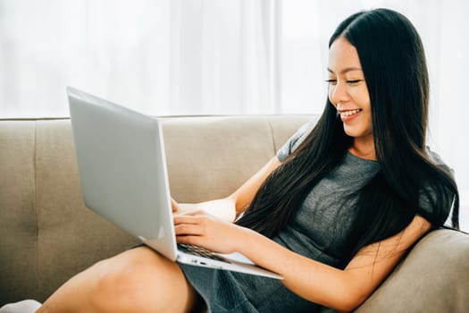 Woman on sofa uses laptop for ecommerce watching videos learning. Embracing studying success and relaxation at home. Modern technology for education and shopping.