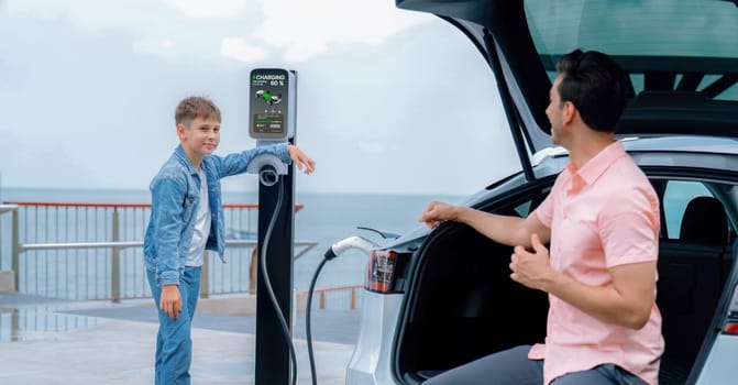 Family road trip vacation traveling by the sea with electric car, father and son recharge EV car with green and clean energy. Natural travel and eco-friendly car for sustainable environment. Perpetual