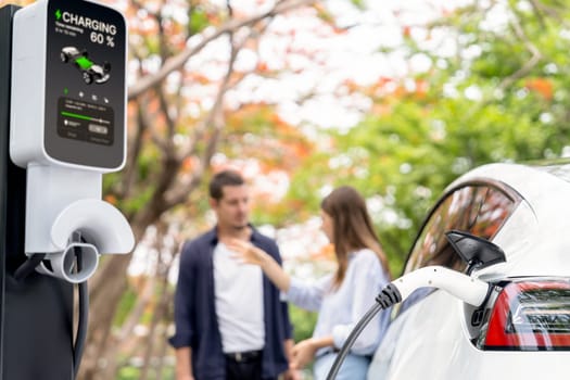 Lovely young couple recharging battery for electric car during autumnal road trip travel EV car in autumnal forest. Eco friendly travel on vacation during autumn. Exalt