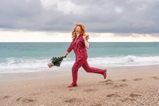 Sea Lady in plaid shirt with a christmas tree in her hands enjoys beach. Coastal area. Christmas, New Year holidays concep.