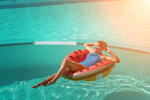Happy woman in a swimsuit and sunglasses floating on an inflatable ring in the form of a watermelon, in the pool during summer holidays and vacations. Summer concept