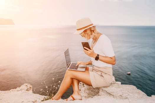 Digital nomad, Business woman working on laptop by the sea. Pretty lady typing on computer by the sea at sunset, makes a business transaction online from a distance. Freelance remote work on vacation