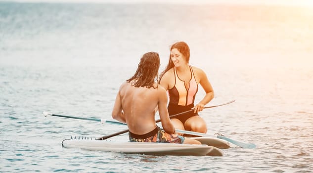 Sea woman and man on sup. Silhouette of happy young woman and man, surfing on SUP board, confident paddling through water surface. Idyllic sunset. Active lifestyle at sea or river