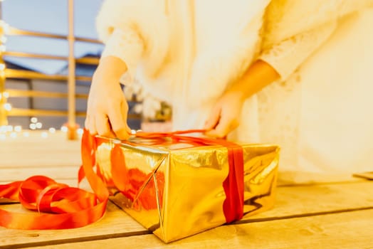 A woman in a white dress is holding a gold box with a red ribbon. She is wearing a crown on her head. The scene takes place in a room with a door and a window. The woman appears to be opening the gift box.