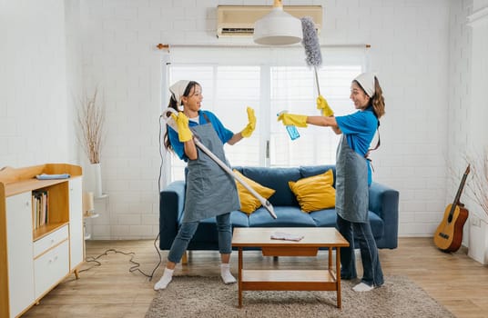 Maid upbeat routine, Asian woman plays vacuum guitar husband playful idea. Singing dancing joyfully. Music-infused service makes housework exciting. Cleaning is fun