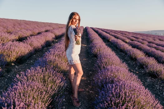 Close up portrait of young beautiful woman in a white dress and a hat is walking in the lavender field and smelling lavender bouquet.