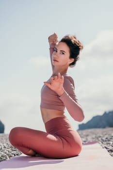 Young woman with long hair in white swimsuit and boho style braclets practicing outdoors on yoga mat by the sea on a sunset. Women's yoga fitness routine. Healthy lifestyle, harmony and meditation