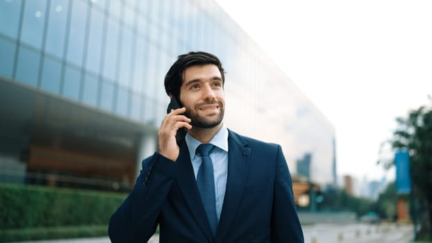 Skilled caucasian project manager calling phone while walking at city with blurred background. Skilled businessman using smart phone talking to project manager with blurred background. Exultant.