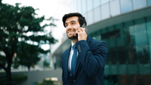 Skilled caucasian project manager calling phone while walking at city with blurred background. Skilled businessman using smart phone talking to project manager with blurred background. Exultant.