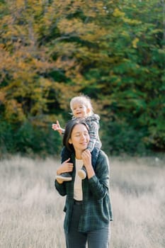 Mom with a little girl on her shoulders stands with her eyes closed in a clearing in the forest. High quality photo