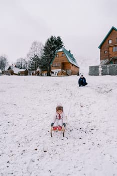 Dad squats on a hill watching a little girl go down on a sled. High quality photo
