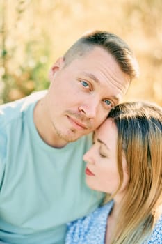 Guy touches girl head with his cheek while hugging her while sitting on the grass. High quality photo