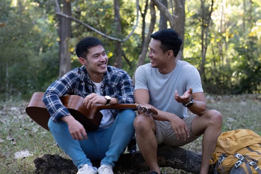 Asian LGBTQ couple enjoying nature, camping with tents in the forest area by the river, playing guitar..